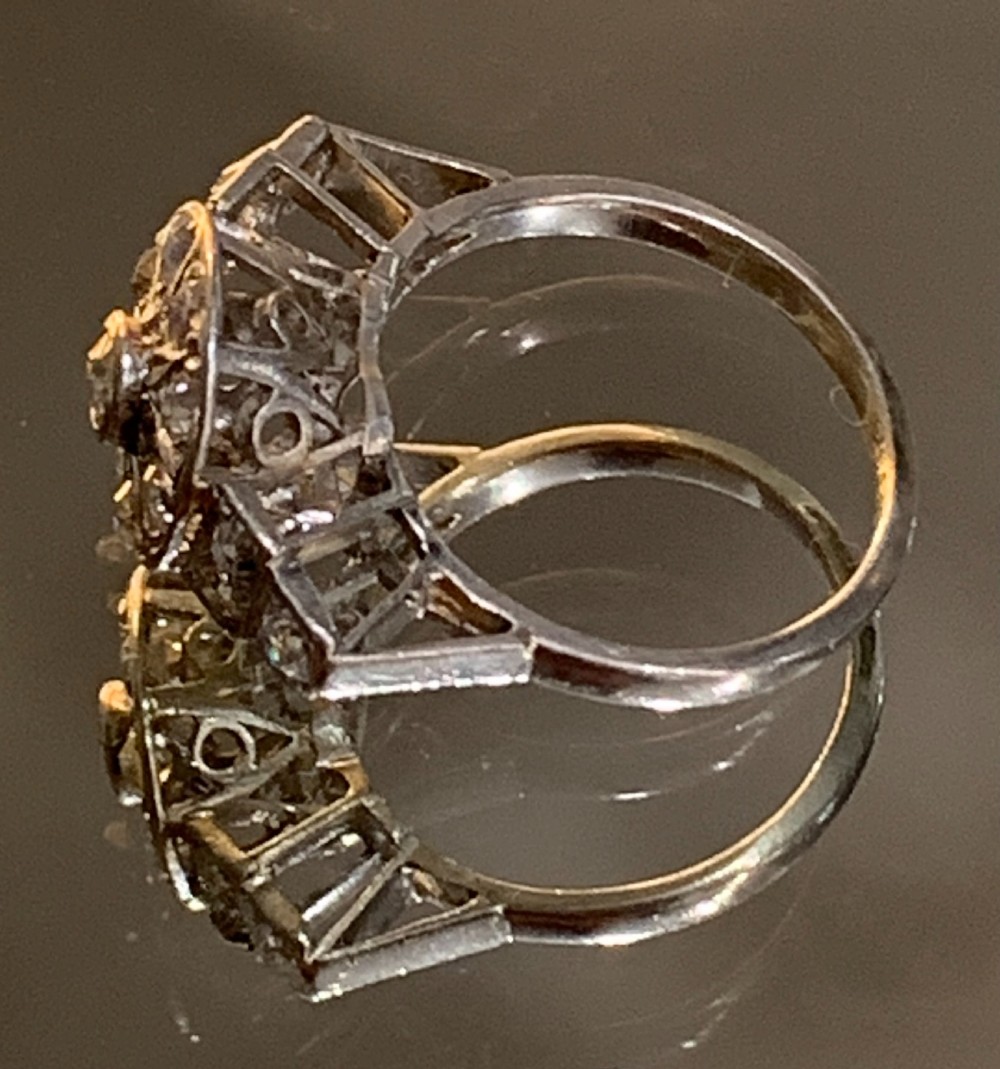 An Art Deco platinum cluster ring featuring a central round diamond framed by smaller diamonds in a geometric starburst setting with stepped shoulders. View V