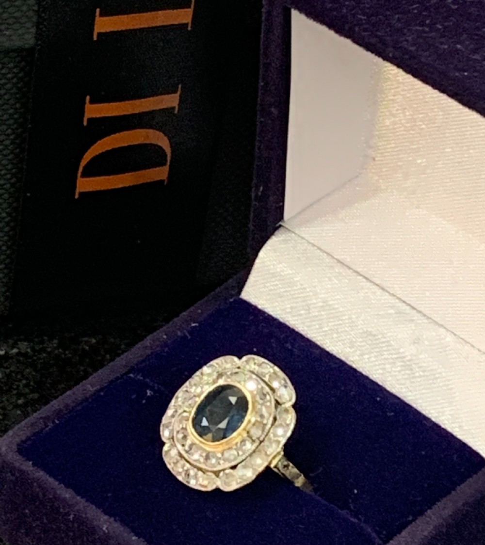 An Art Deco cluster ring featuring a central oval blue sapphire surrounded by a double halo of small diamonds set on a yellow gold band. View V