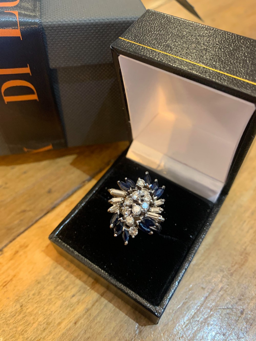 An 18ct white gold cluster ring set with round brilliant diamonds, baguette diamonds, and marquise-cut blue sapphires in a starburst arrangement.