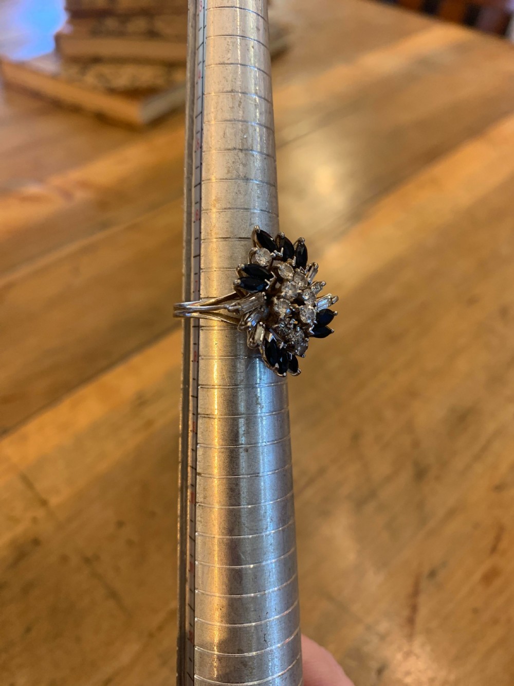 An 18ct white gold cluster ring set with round brilliant diamonds, baguette diamonds, and marquise-cut blue sapphires in a starburst arrangement. View III
