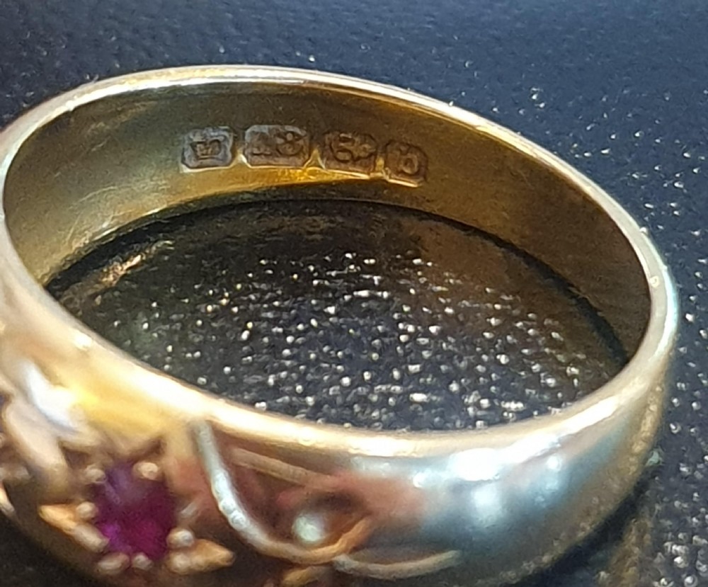 An Edwardian yellow gold band ring featuring a central blue sapphire flanked by two red rubies set in star-shaped recessed mountings. View II
