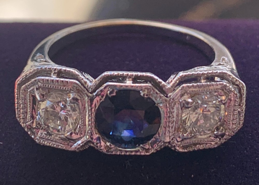 An Art Deco three-stone ring featuring a central blue sapphire flanked by two diamonds set in octagonal millegrain mounts.
