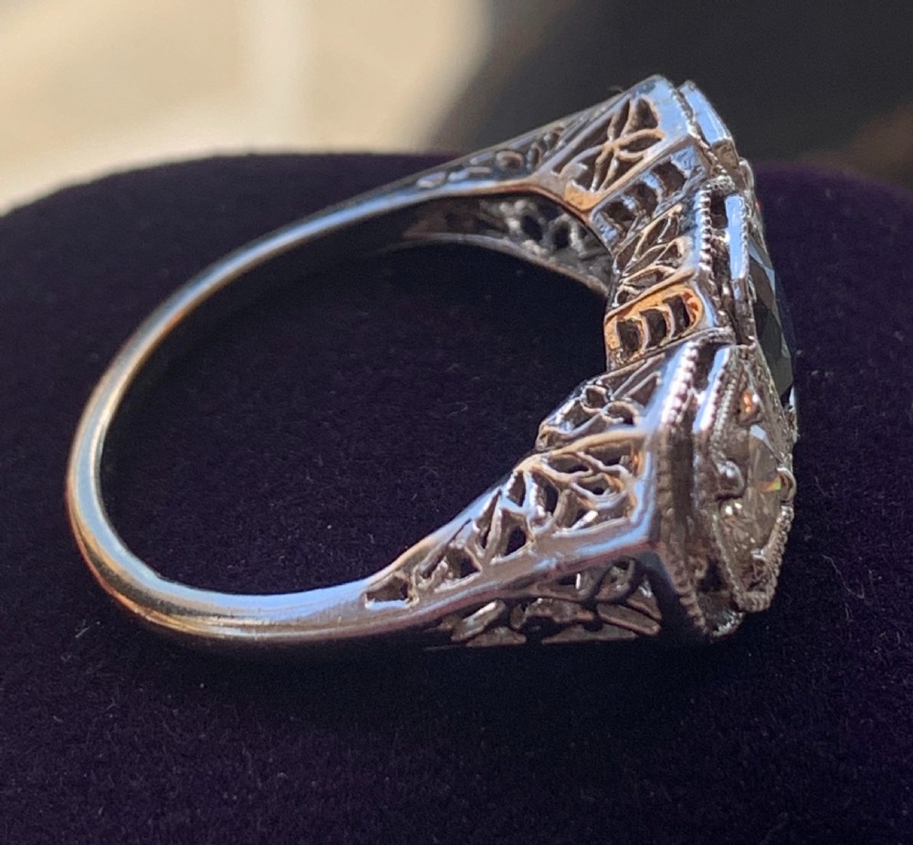 An Art Deco three-stone ring featuring a central blue sapphire flanked by two diamonds set in octagonal millegrain mounts. View III