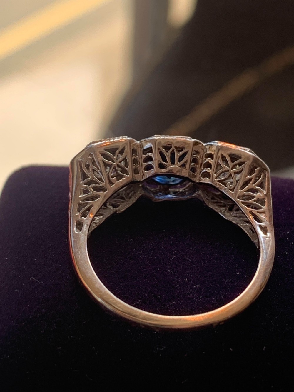 An Art Deco three-stone ring featuring a central blue sapphire flanked by two diamonds set in octagonal millegrain mounts. View V