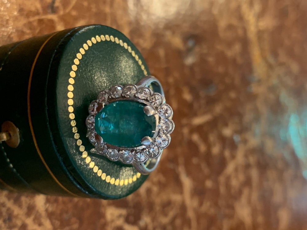 An Art Deco platinum cluster ring featuring an oval green emerald surrounded by a halo of brilliant-cut diamonds. View IV