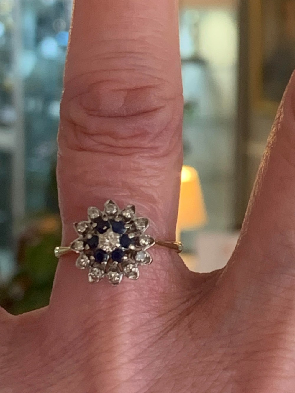 An antique target cluster ring featuring a central round diamond framed by deep blue sapphires and an outer halo of diamonds in platinum on an 18ct gold band. View VI