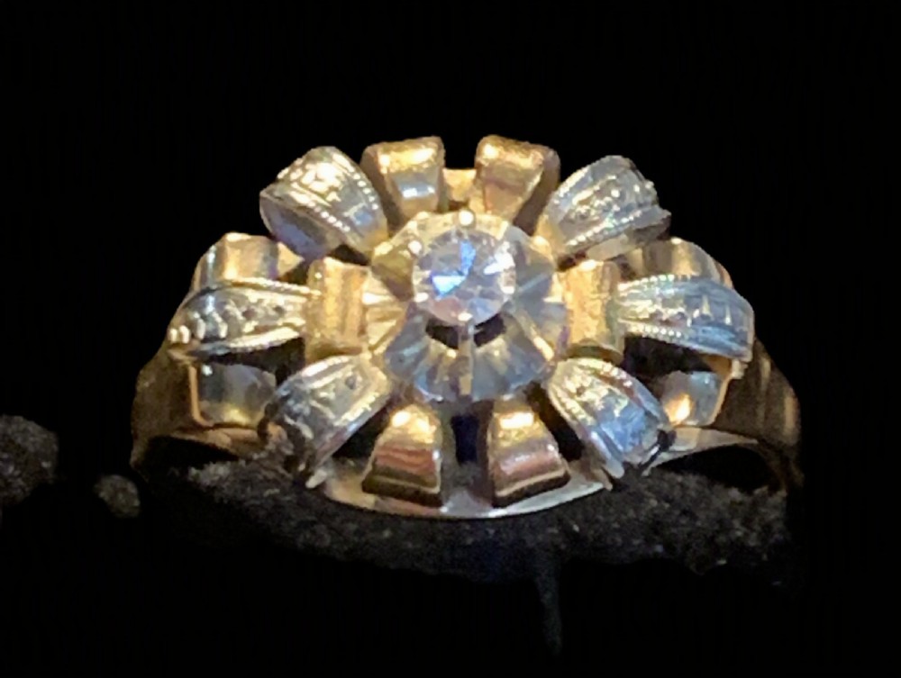 An Art Deco 18ct gold ring featuring a central round diamond surrounded by a textured ribbon cluster motif.
