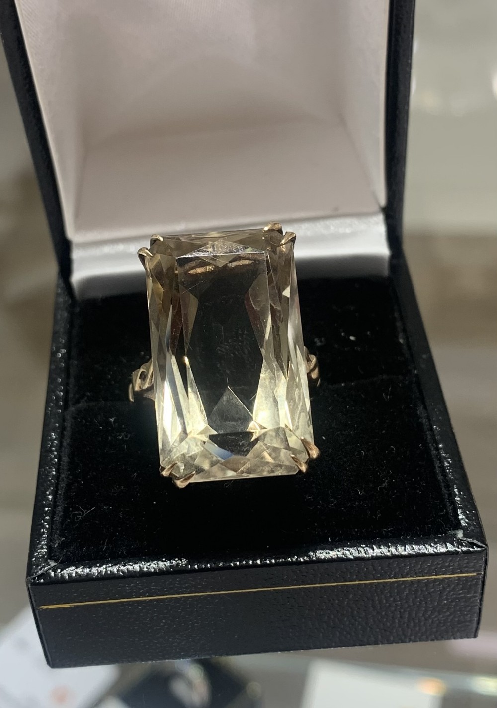 A large rectangular step-cut smoky quartz gemstone mounted in a yellow gold claw setting within a black presentation box.