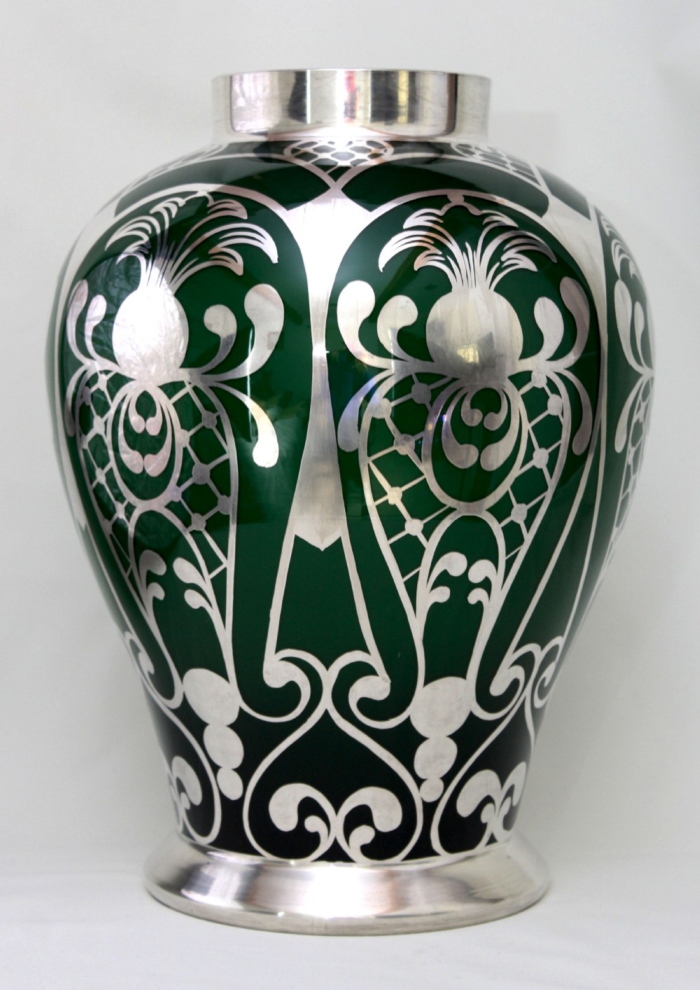 A deep green glass vase adorned with intricate sterling silver overlay featuring stylised foliage and lattice patterns.