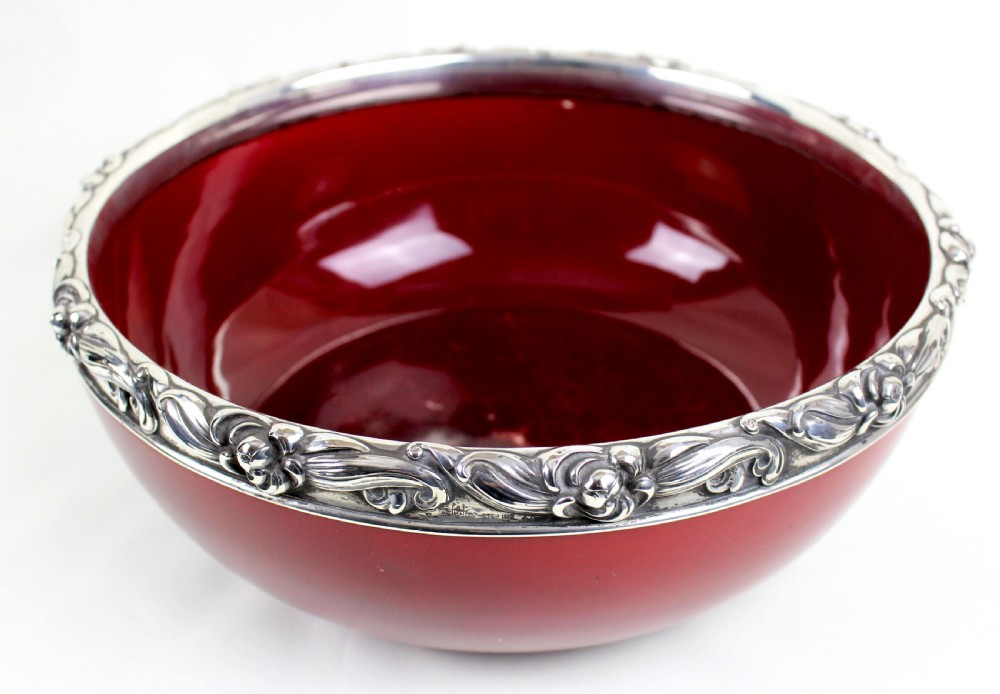 A deep circular red flambe ceramic bowl featuring a thick repousse sterling silver rim with floral and scroll reliefs.