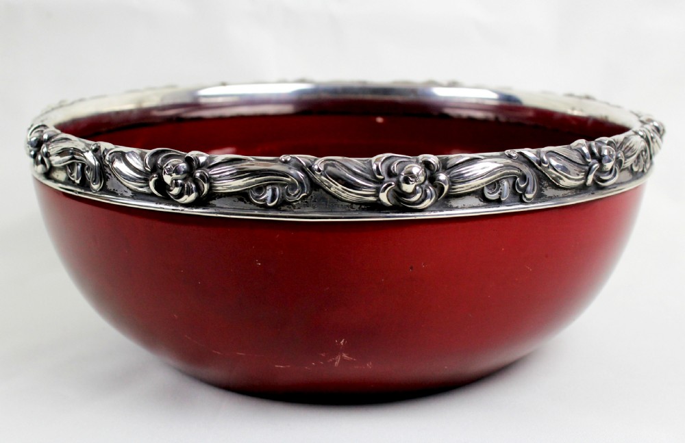 A deep circular red flambe ceramic bowl featuring a thick repousse sterling silver rim with floral and scroll reliefs. View II
