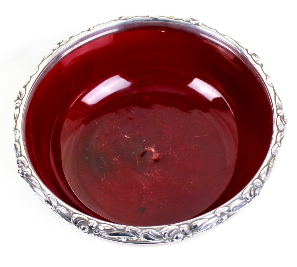 A deep circular red flambe ceramic bowl featuring a thick repousse sterling silver rim with floral and scroll reliefs. View IV