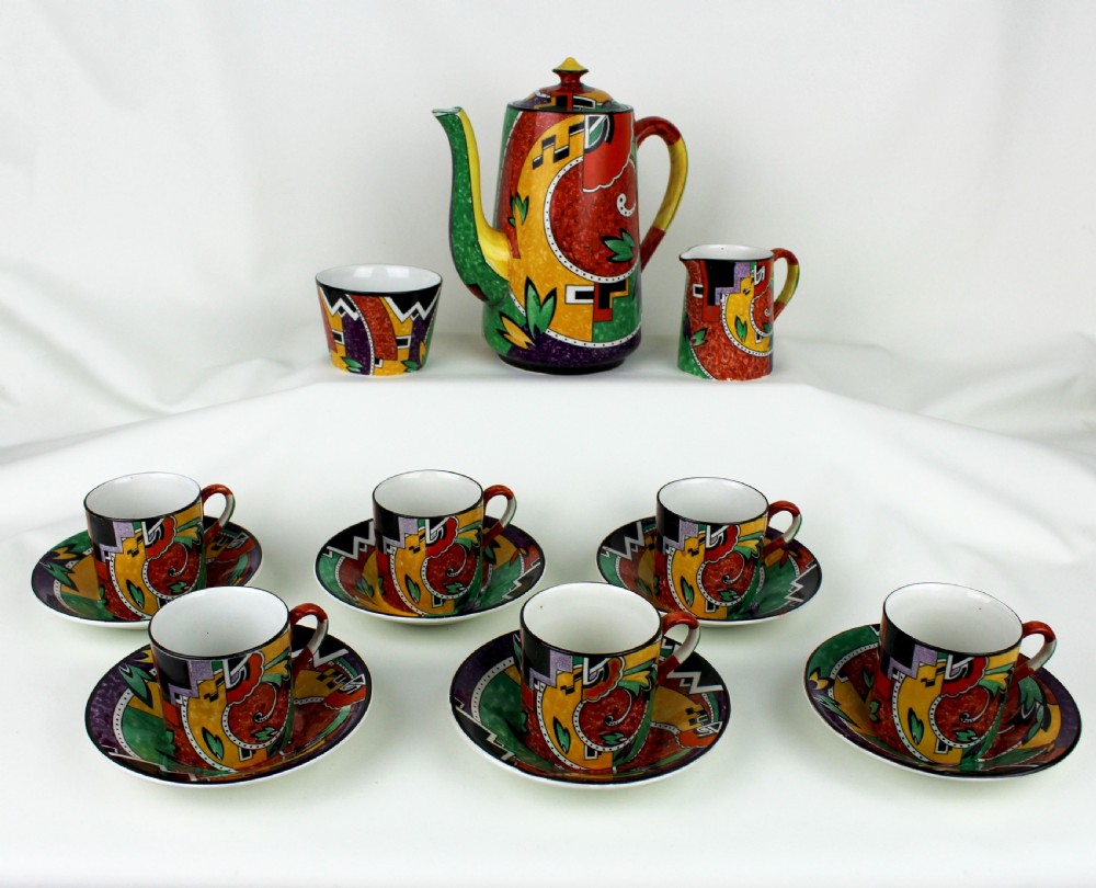 A multi-piece Art Deco ceramic coffee set decorated with vibrant red, yellow, green, and black abstract geometric patterns, comprising a tall coffee pot, creamer, sugar bowl, six demitasse cups, and matching saucers.