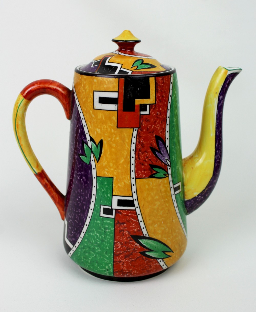 A multi-piece Art Deco ceramic coffee set decorated with vibrant red, yellow, green, and black abstract geometric patterns, comprising a tall coffee pot, creamer, sugar bowl, six demitasse cups, and matching saucers. View VI