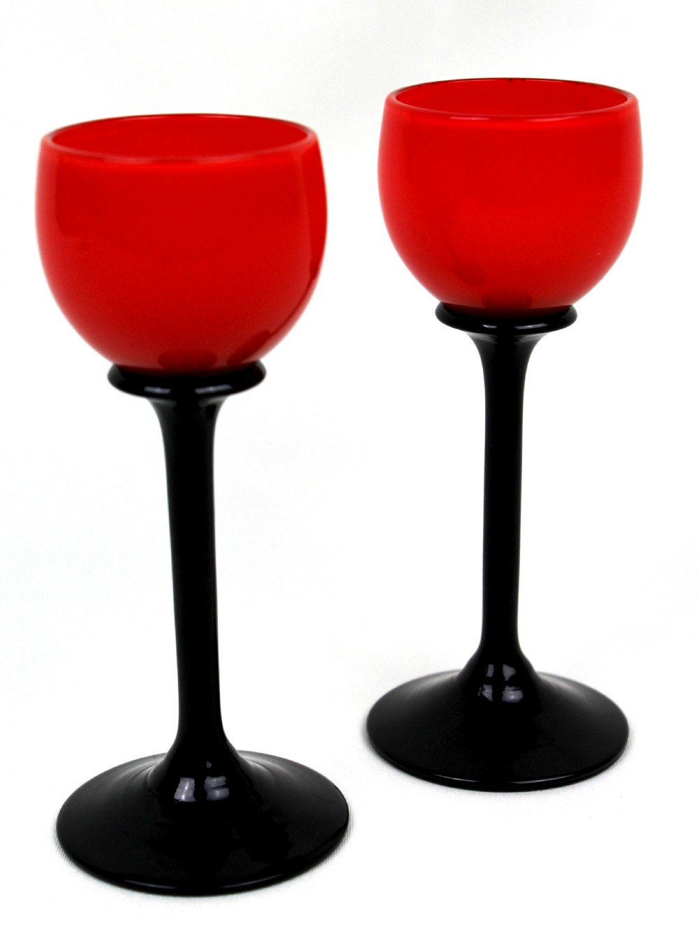 A pair of Art Deco Tango liqueur glasses featuring bright red rounded bowls supported by slender black stems and flat circular black bases.