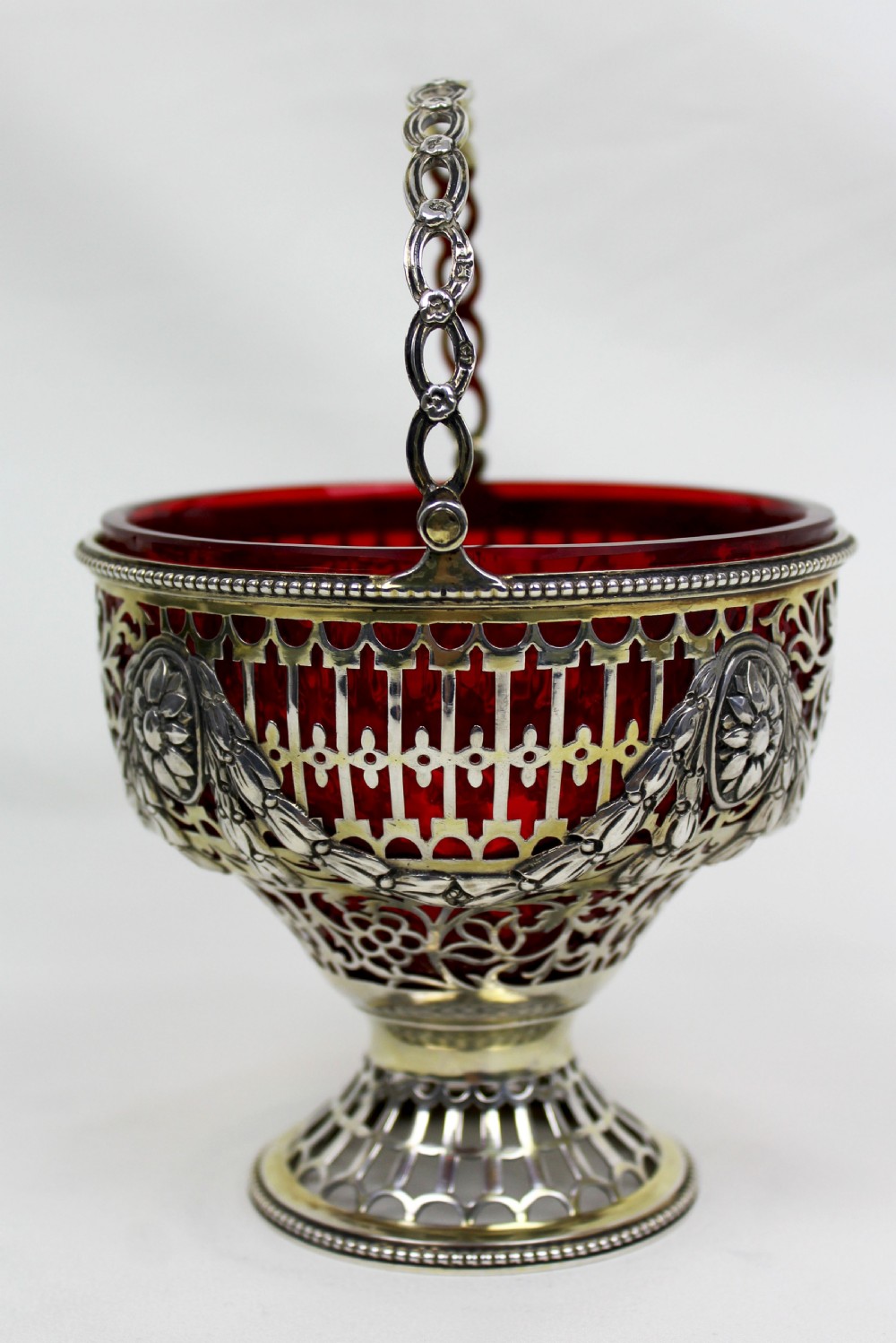 A Victorian silver-gilt sugar basket featuring elaborate pierced openwork, floral swags, a swing handle, and a removable ruby red glass liner. View II