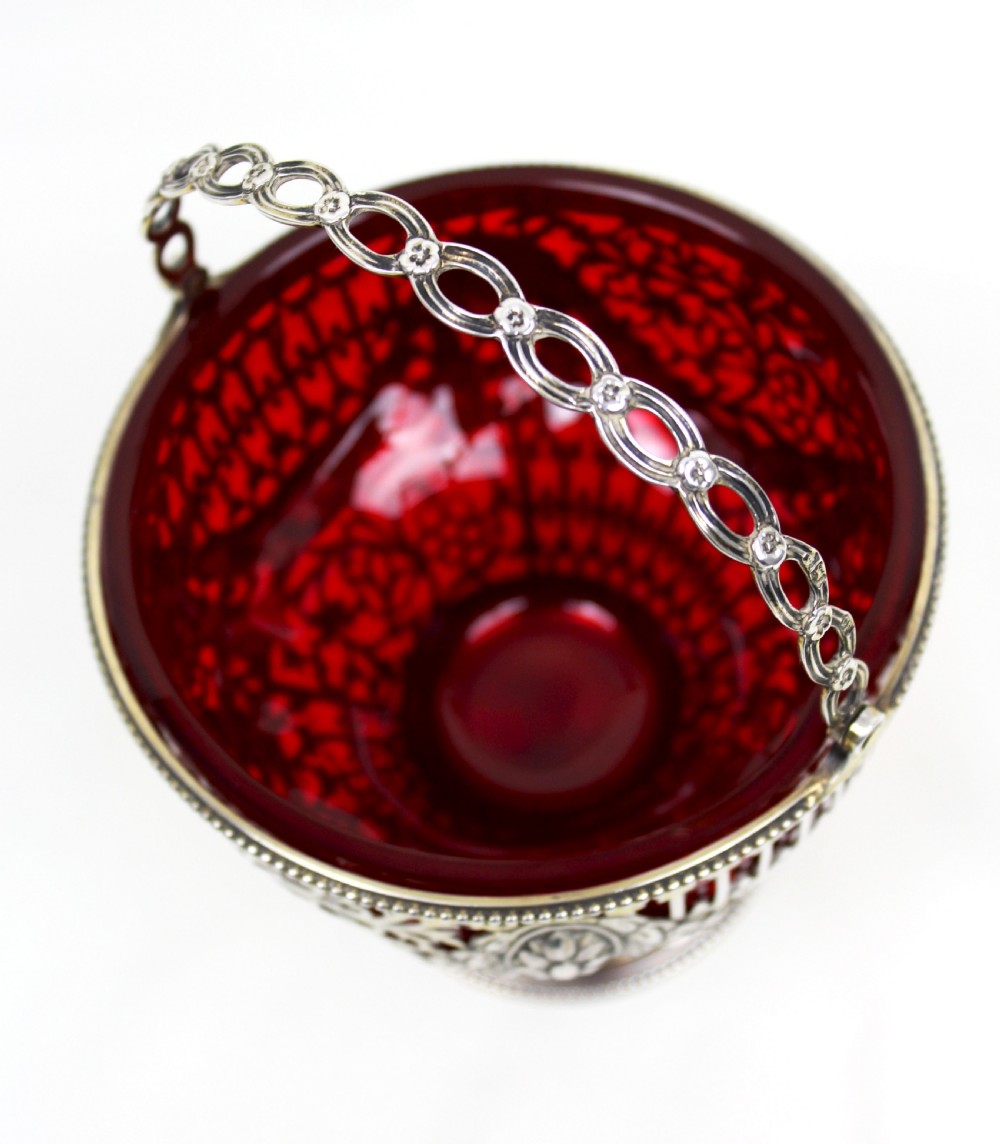 A Victorian silver-gilt sugar basket featuring elaborate pierced openwork, floral swags, a swing handle, and a removable ruby red glass liner. View IV