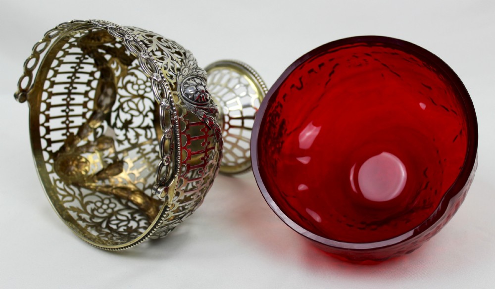 A Victorian silver-gilt sugar basket featuring elaborate pierced openwork, floral swags, a swing handle, and a removable ruby red glass liner. View V
