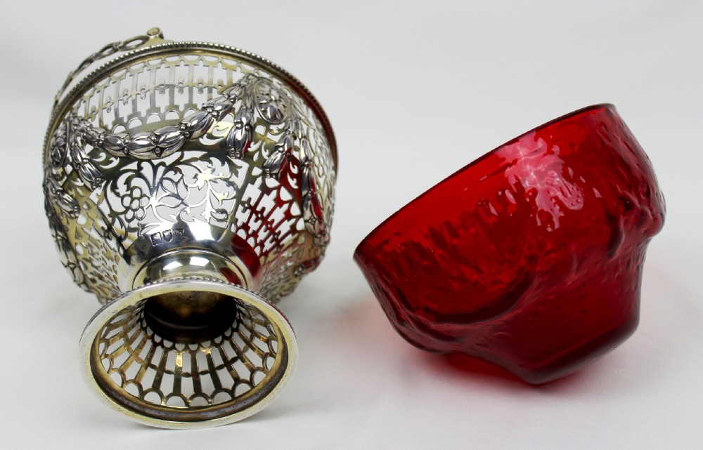 A Victorian silver-gilt sugar basket featuring elaborate pierced openwork, floral swags, a swing handle, and a removable ruby red glass liner. View VI