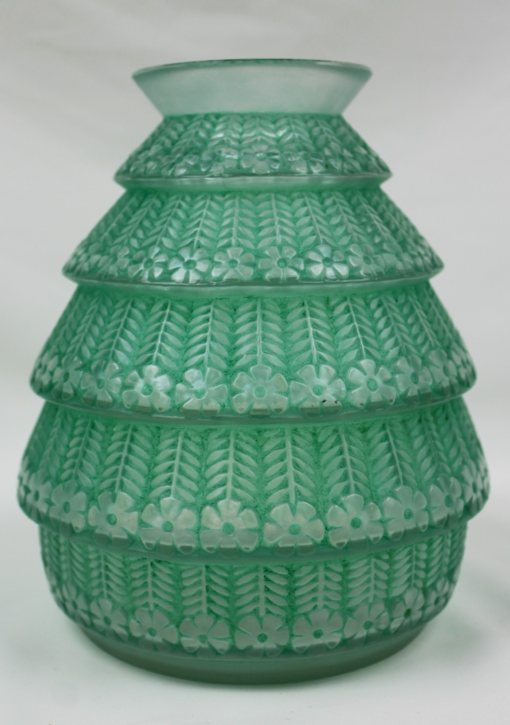 A green frosted glass Art Deco vase featuring tiered conical bands decorated with relief floral and leaf patterns.