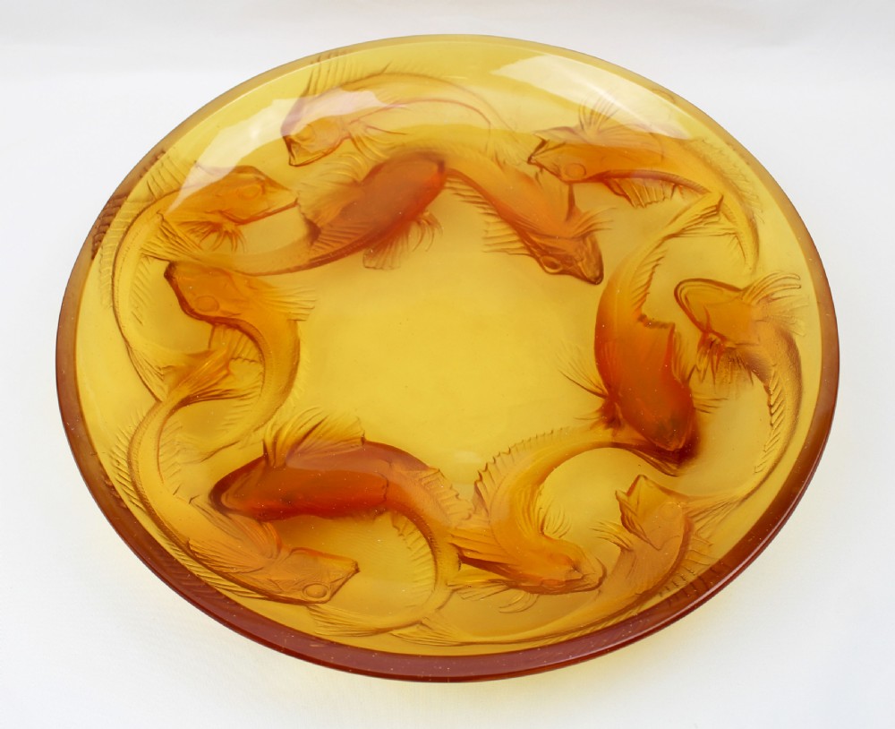 An Art Deco amber glass shallow dish featuring a relief motif of swimming fish radiating around the centre.