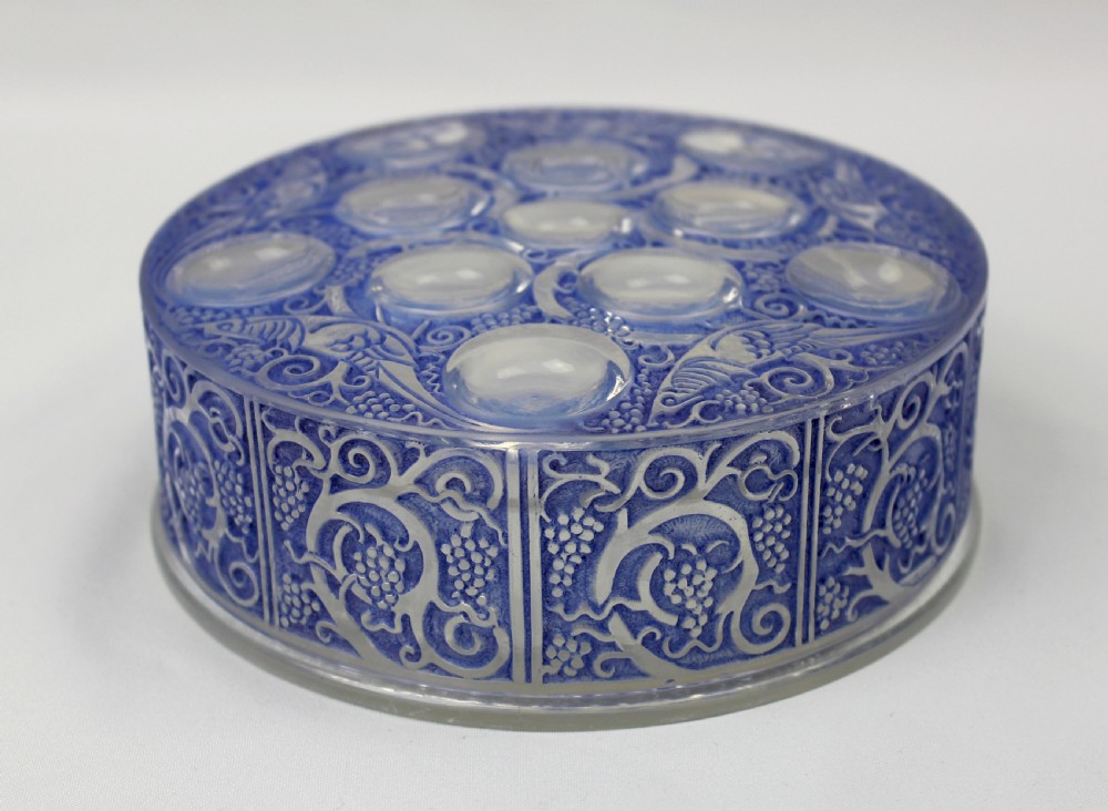 A circular Art Deco blue-stained glass powder box featuring moulded relief patterns of birds, grapevines, and polished glass cabochons.