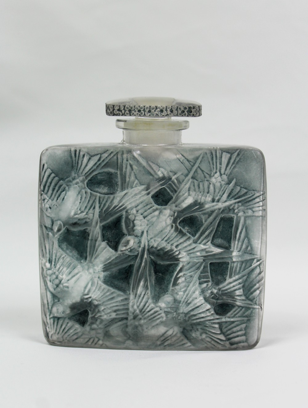 A rectangular frosted glass perfume bottle featuring relief carvings of flying swallows and a matching flat stopper.