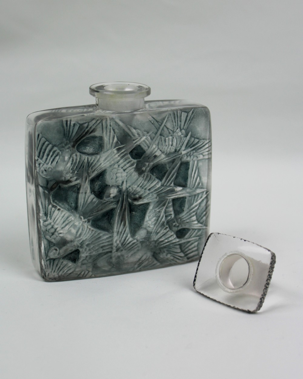 A rectangular frosted glass perfume bottle featuring relief carvings of flying swallows and a matching flat stopper. View III