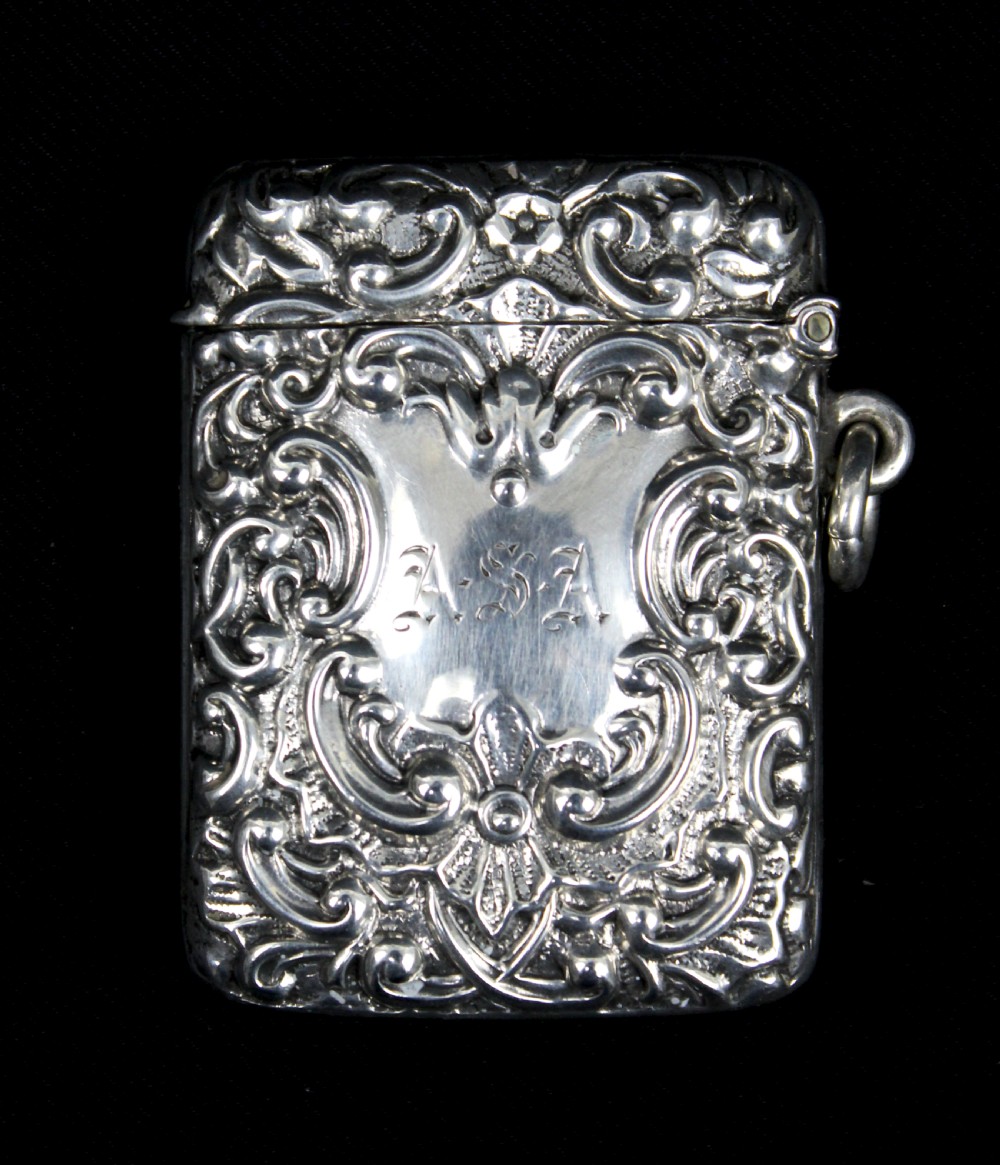 An ornate rectangular sterling silver Vesta case featuring embossed scrollwork and a central engraved cartouche with initials.