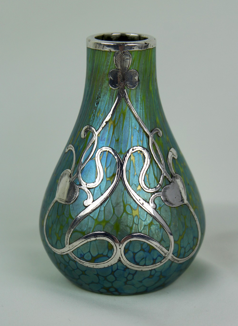 An iridescent blue and green glass vase featuring intricate silver overlay in a swirling Art Nouveau trefoil pattern.