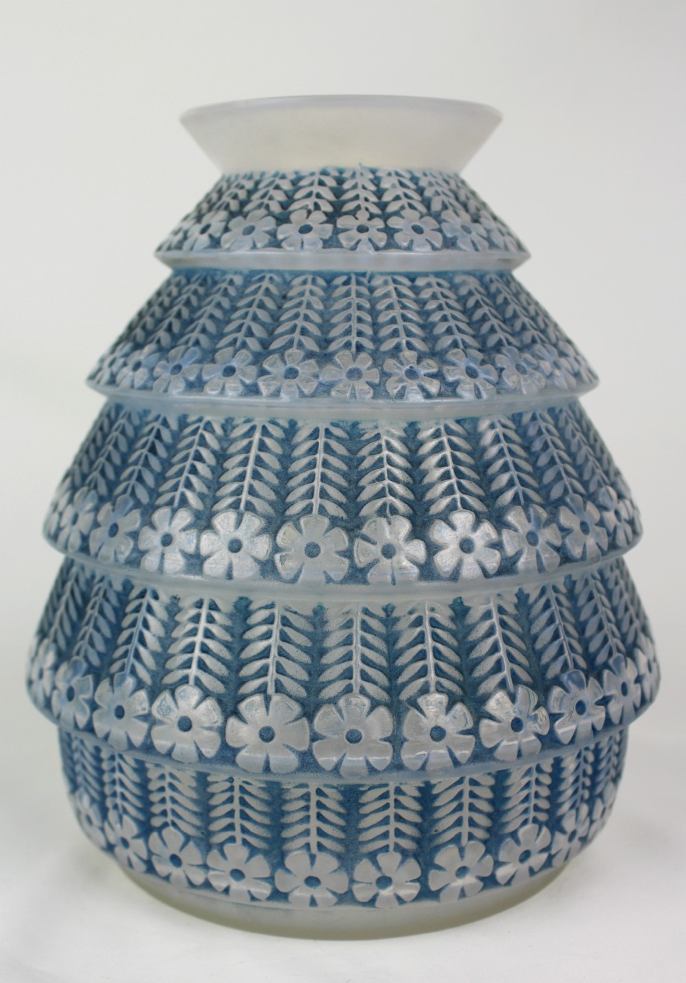 A conical frosted glass vase featuring stepped tiers with relief-moulded floral and leaf motifs highlighted in blue staining.