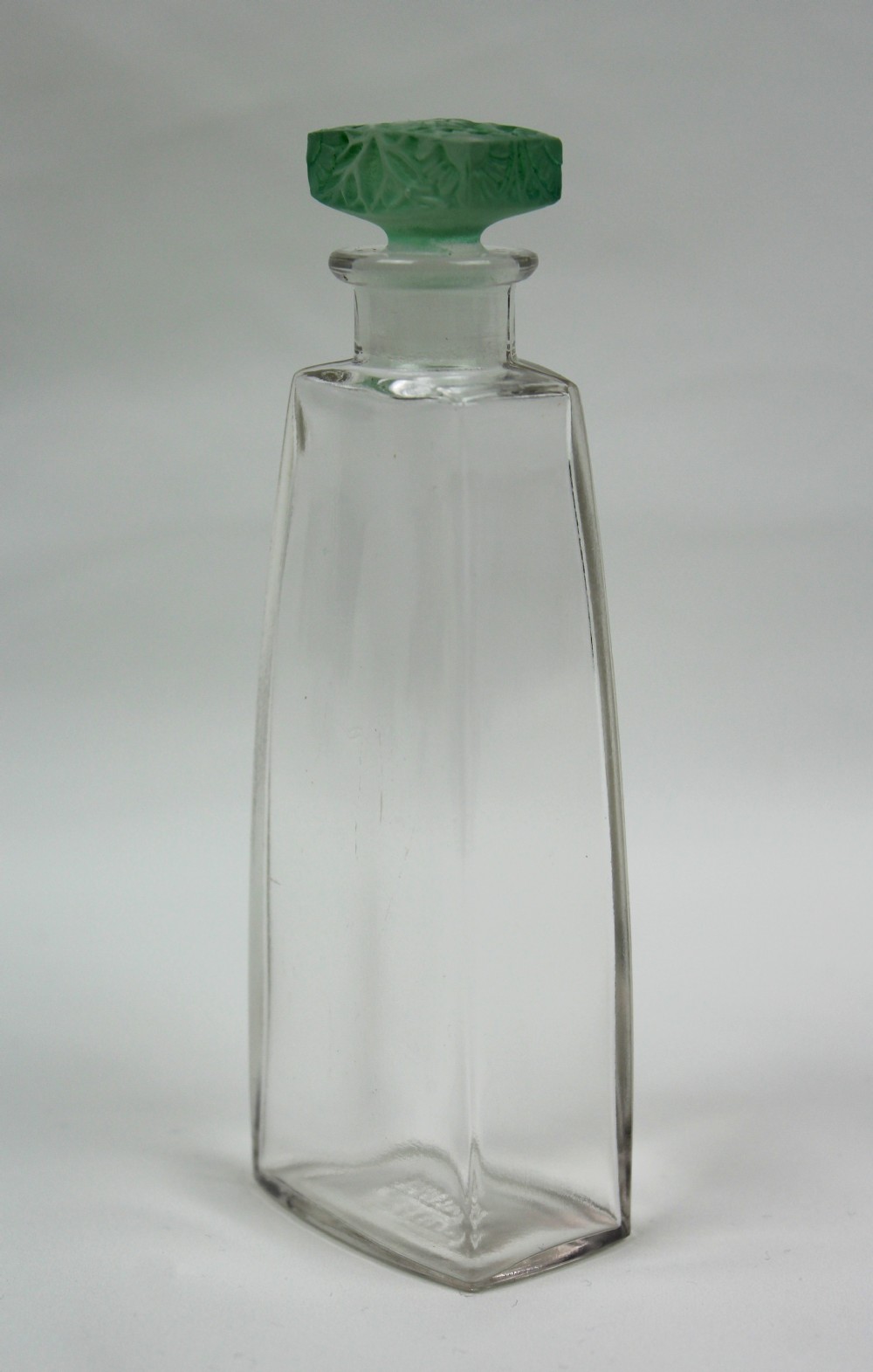 A clear glass Art Deco perfume bottle with a tapered rectangular body and a green frosted glass stopper decorated with a carved leaf pattern. View II