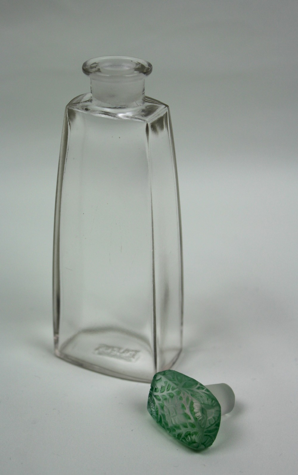 A clear glass Art Deco perfume bottle with a tapered rectangular body and a green frosted glass stopper decorated with a carved leaf pattern. View III