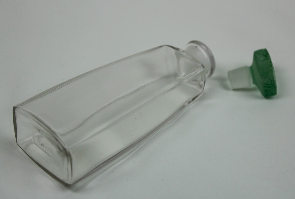 A clear glass Art Deco perfume bottle with a tapered rectangular body and a green frosted glass stopper decorated with a carved leaf pattern. View IV