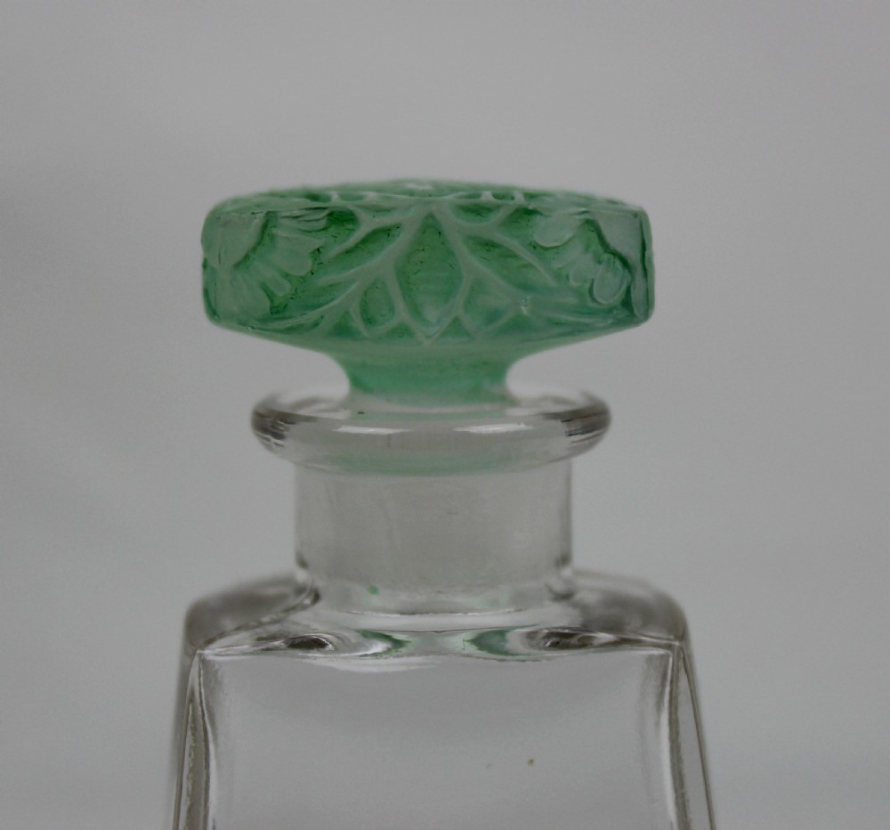 A clear glass Art Deco perfume bottle with a tapered rectangular body and a green frosted glass stopper decorated with a carved leaf pattern. View VI