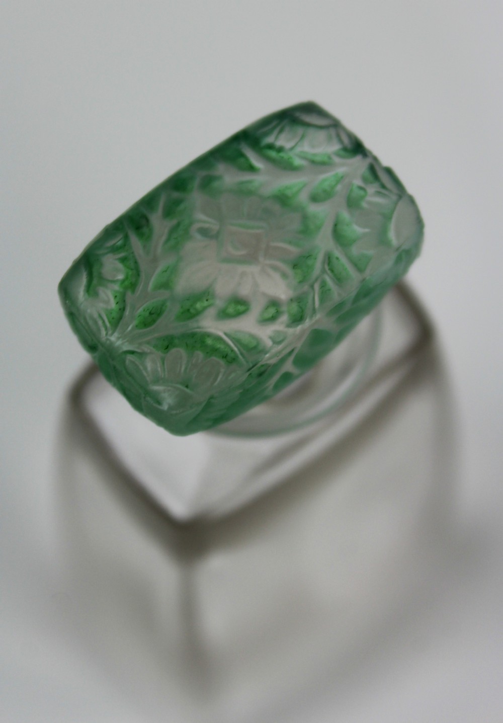 A clear glass Art Deco perfume bottle with a tapered rectangular body and a green frosted glass stopper decorated with a carved leaf pattern. View VII