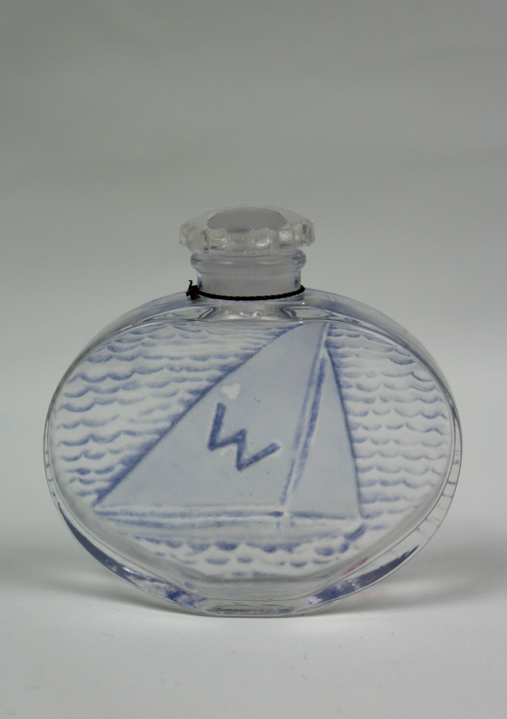 An oval clear glass scent bottle featuring a moulded sailboat on ocean waves accentuated with blue stain, topped with a faceted stopper. View II