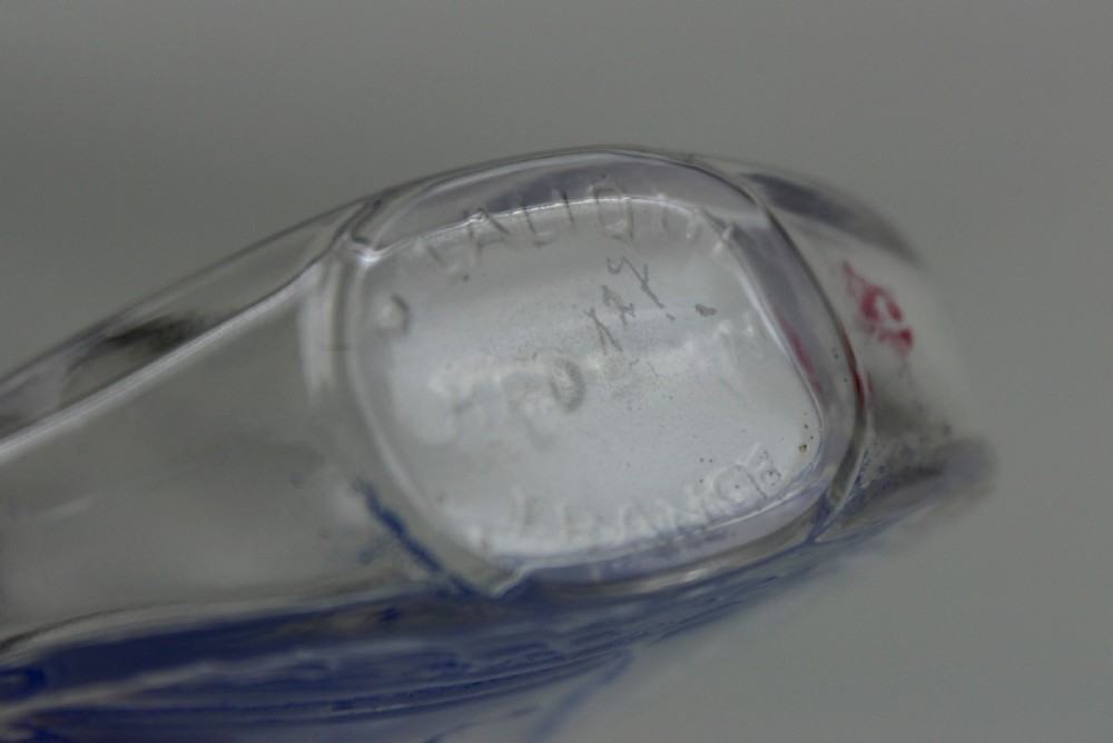 An oval clear glass scent bottle featuring a moulded sailboat on ocean waves accentuated with blue stain, topped with a faceted stopper. View VI