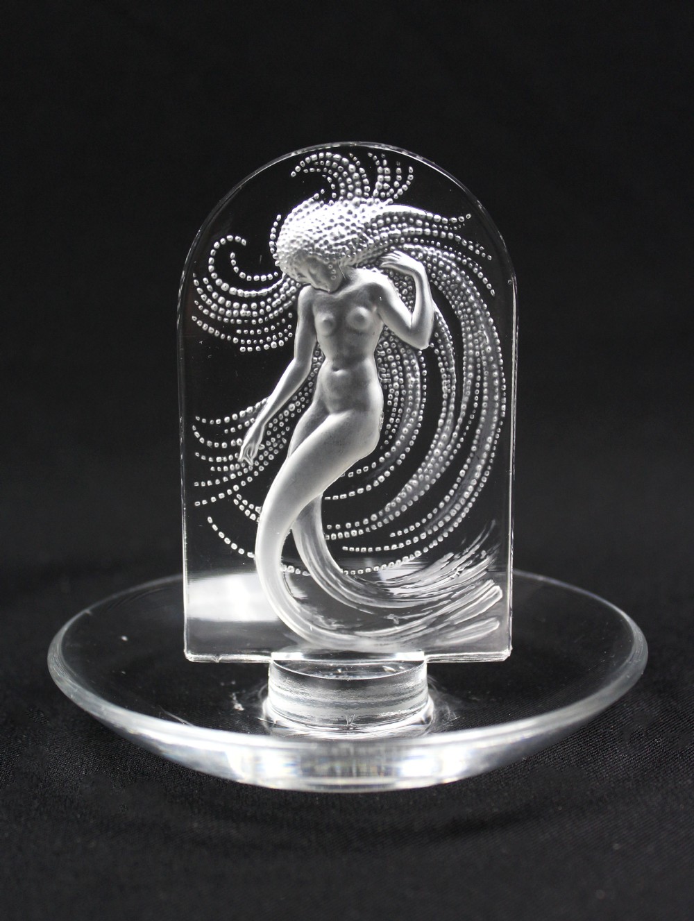 A clear glass pin dish featuring an upright arched centrepiece with a frosted glass relief depiction of a nymph surrounded by swirling beaded patterns.