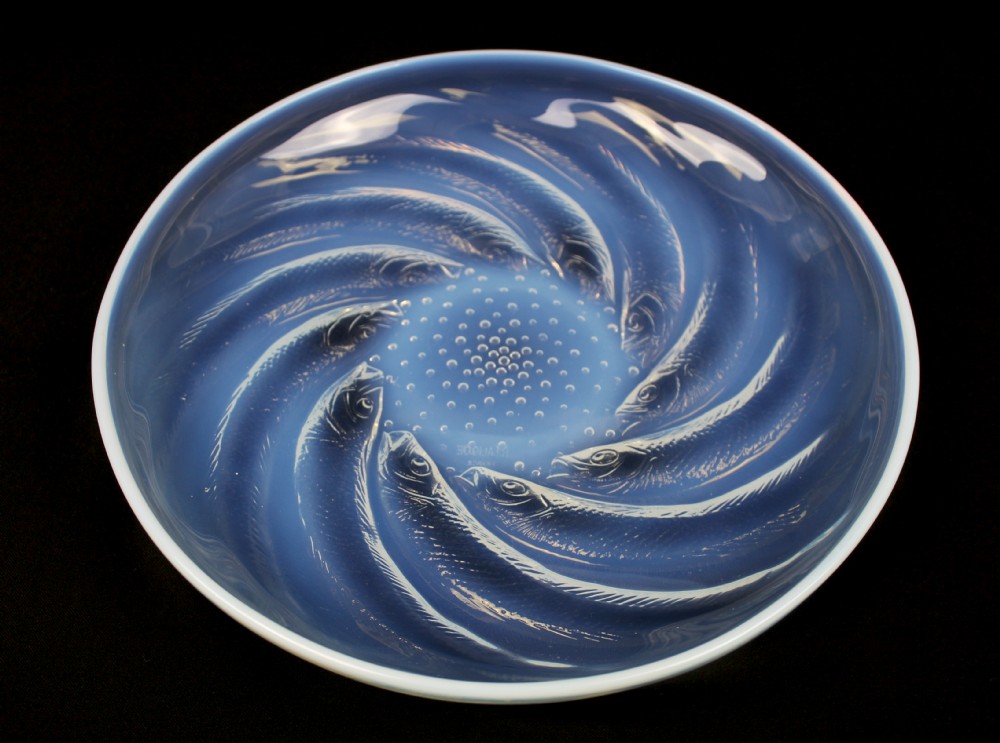 A circular Art Deco opalescent blue glass plate decorated with a swirling relief design of fish radiating from a central field of small raised bubbles.