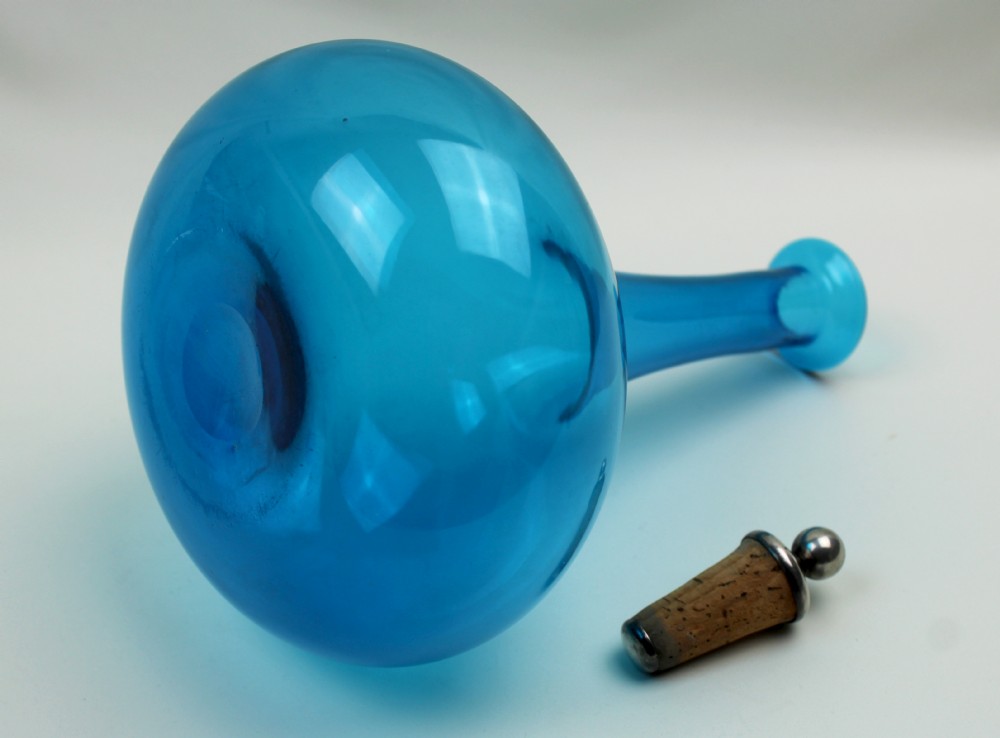 A vibrant blue hand-blown glass mell decanter with a rounded base, slender neck, and a cork stopper topped with a silver spherical finial. View III