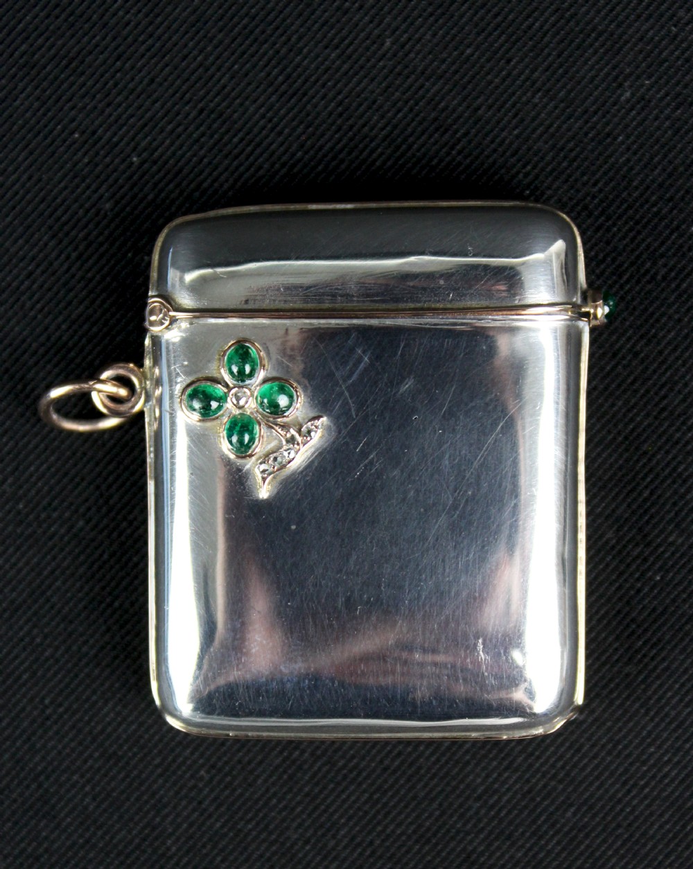 An antique rectangular sterling silver vesta case featuring gold trim, a side attachment loop, and a shamrock motif set with green cabochon gemstones and diamonds.
