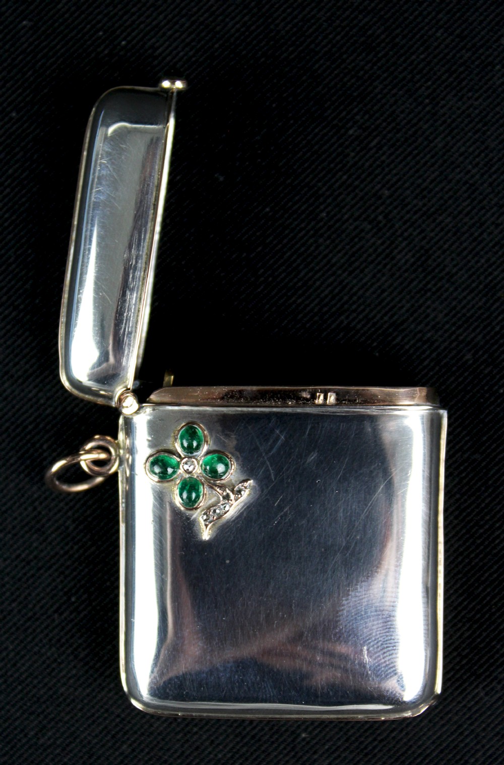 An antique rectangular sterling silver vesta case featuring gold trim, a side attachment loop, and a shamrock motif set with green cabochon gemstones and diamonds. View III