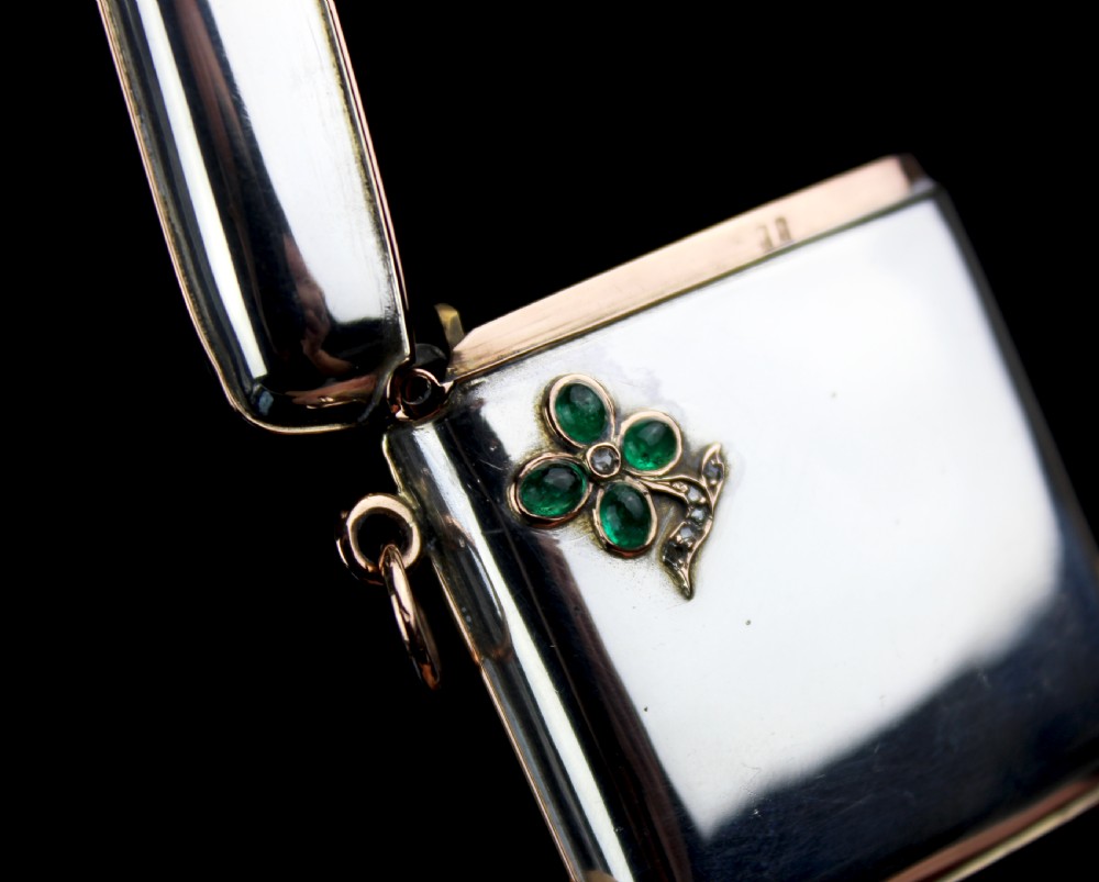 An antique rectangular sterling silver vesta case featuring gold trim, a side attachment loop, and a shamrock motif set with green cabochon gemstones and diamonds. View IV
