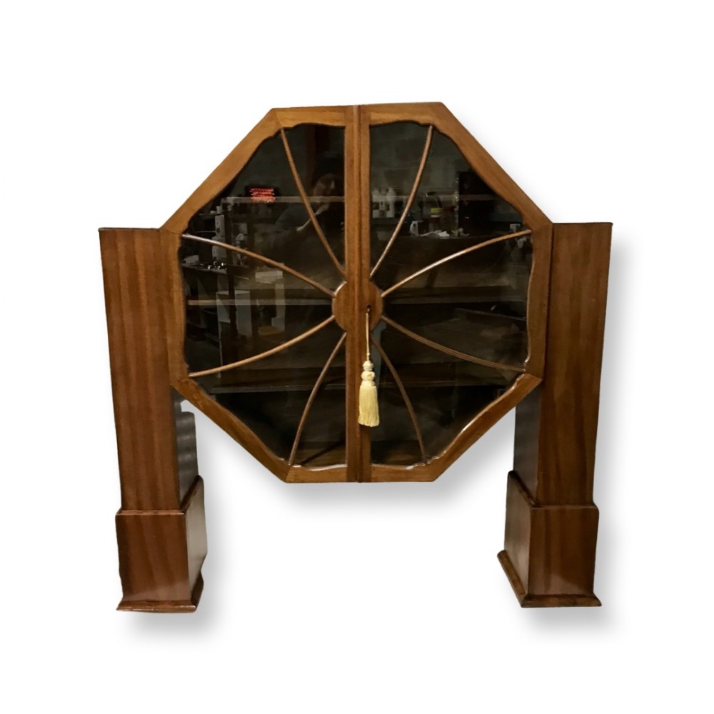 An Art Deco warm brown wood display cabinet featuring an octagonal glazed centre with spider-web astragal glazing bars, flanked by twin rectangular side supports.