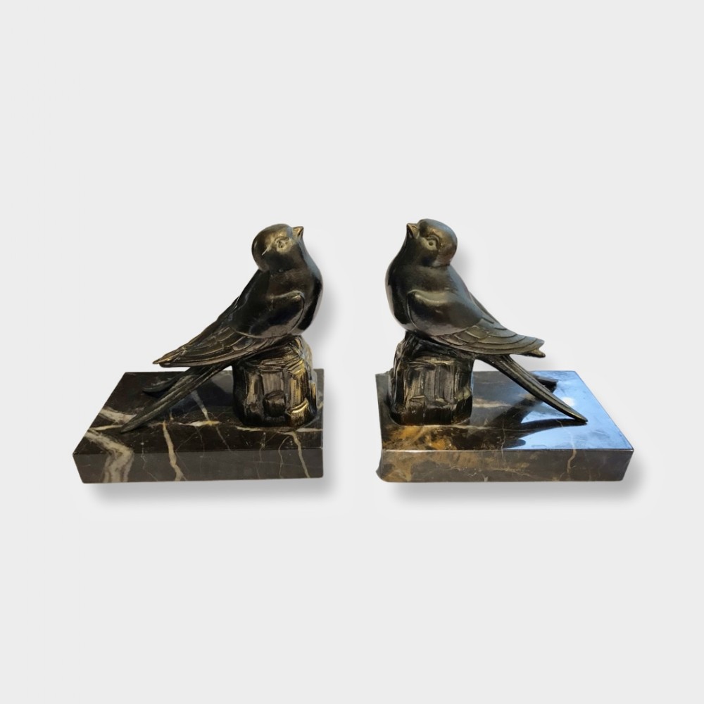 A pair of dark patinated metal swallow sculptures positioned on rectangular black marble bases with white veining.