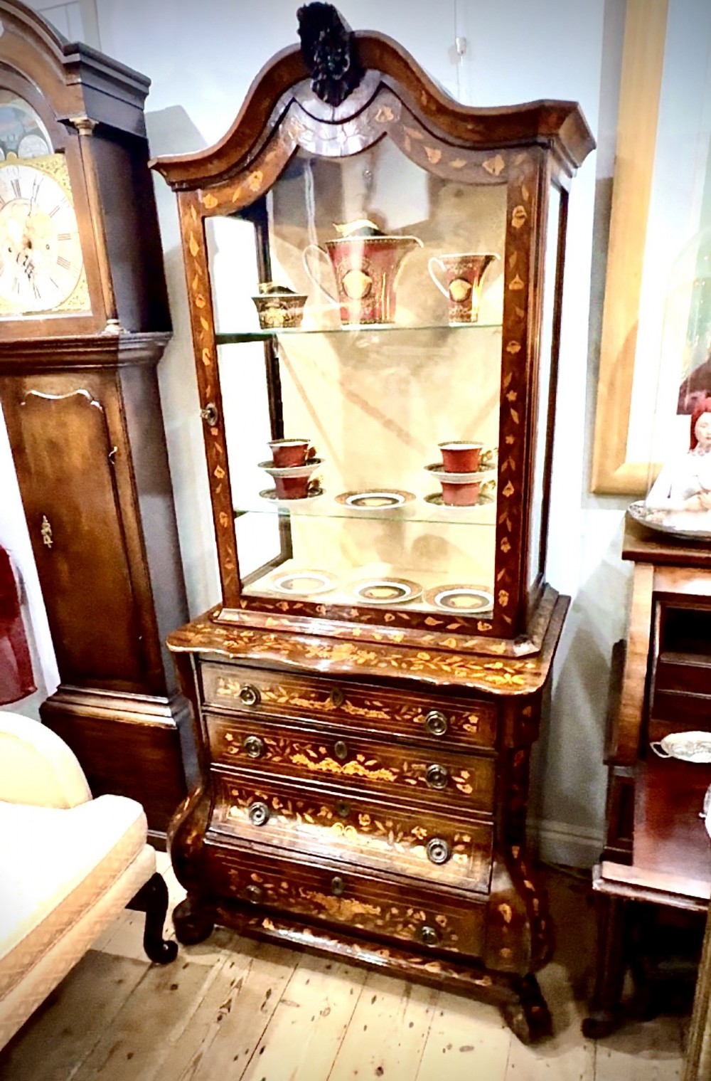 An antique Dutch walnut display cabinet featuring intricate floral wood marquetry, an arched glazed top, and a base with four drawers. View II