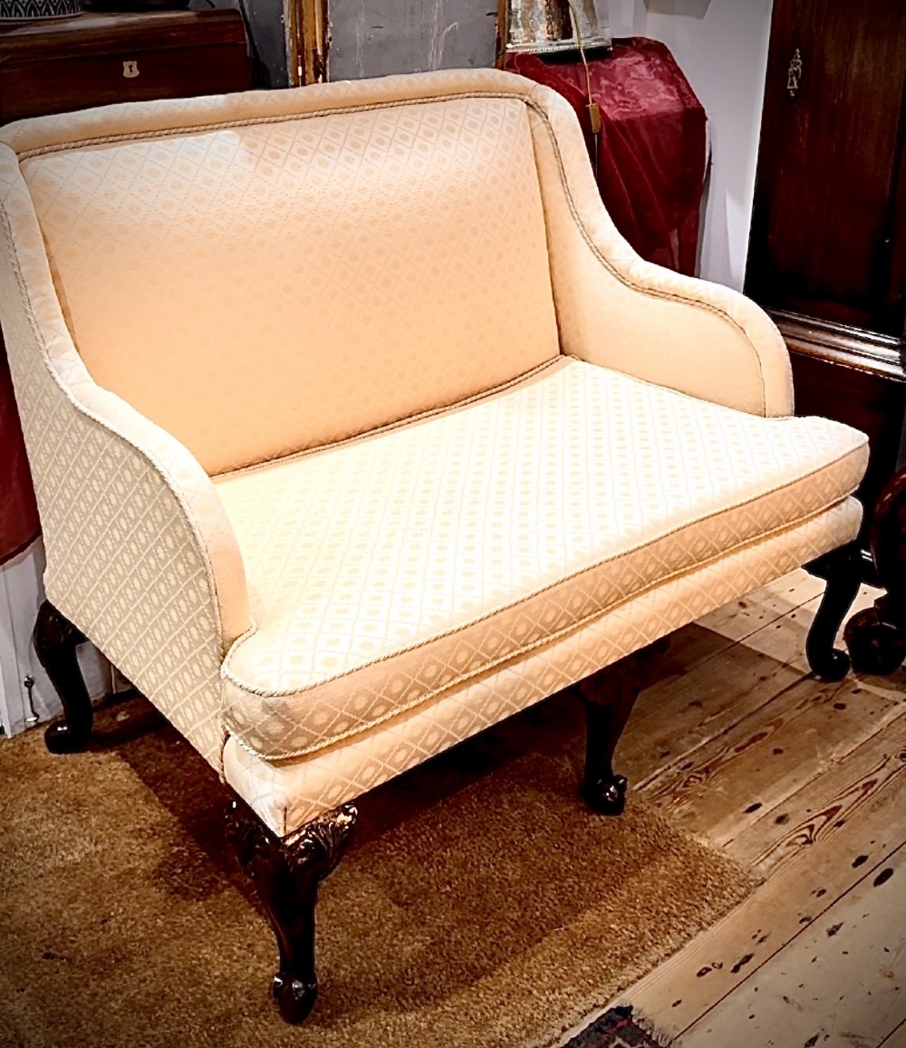 An Edwardian two-seater settee upholstered in cream geometric patterned fabric with piping trim and raised on dark carved mahogany cabriole legs.