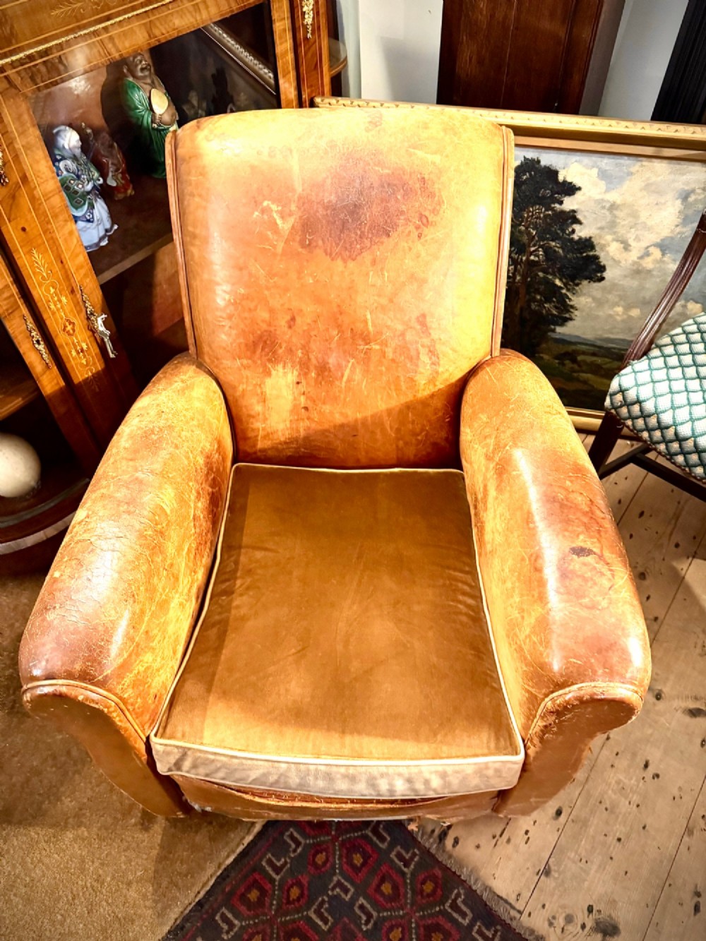 An Art Deco tan leather club chair featuring rolled armrests, distressed leather patina, and a fitted velvet seat cushion. View II