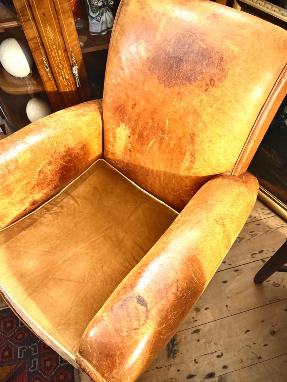 An Art Deco tan leather club chair featuring rolled armrests, distressed leather patina, and a fitted velvet seat cushion. View III